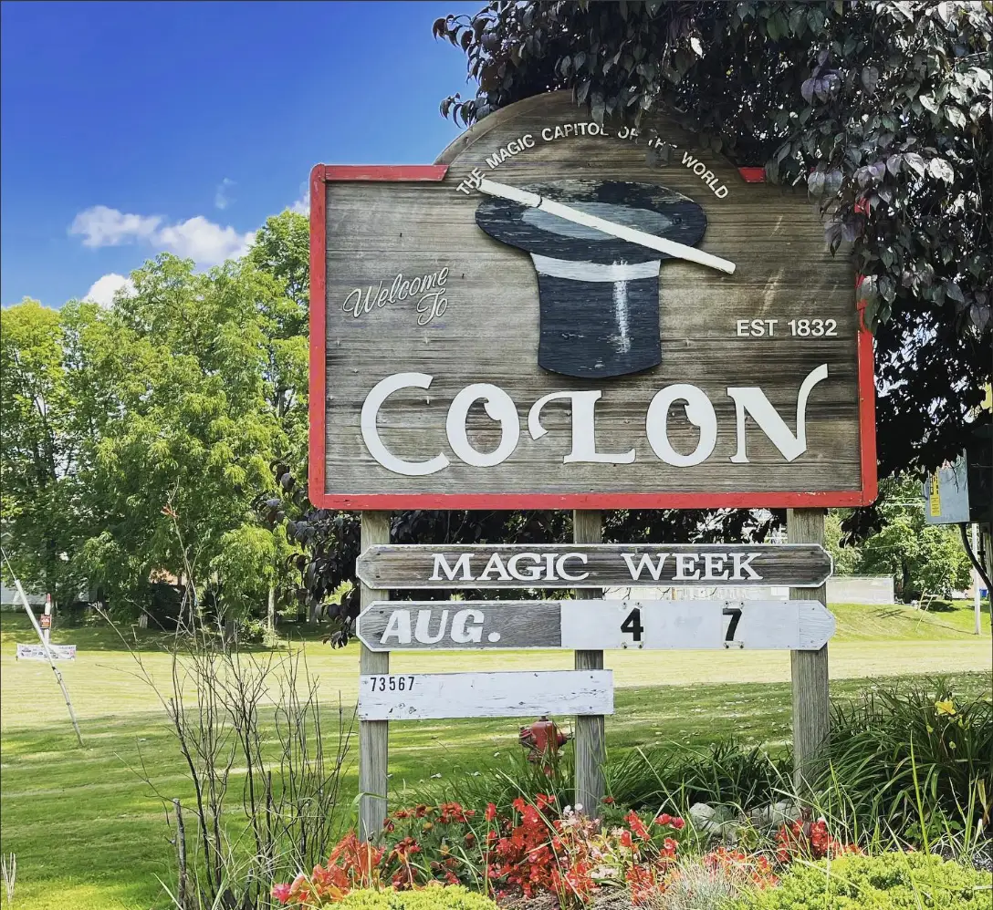 The wooden Welcome to Colon town sign, painted with a top hat and wand, reading The Magic Capitol of the World and Magic Week August 4 to 7