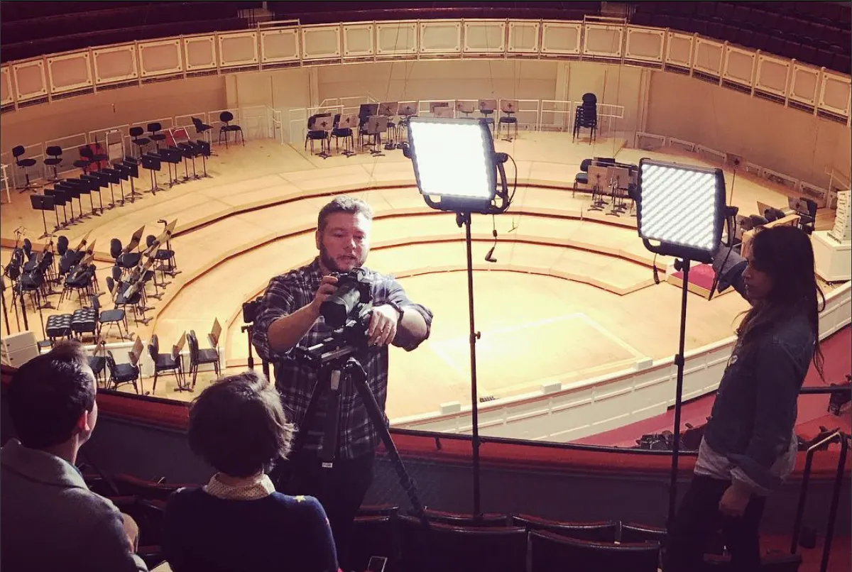 Greg Mulvey operating a camera on a slider in the empty Orchestra Hall at Symphony Center, lights rigged over the stage
